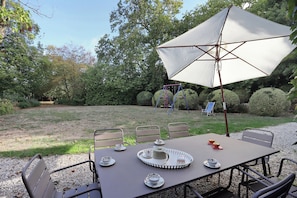 Un espacio de comedor al aire libre con una mesa dispuesta para cuatro personas, rodeada de sillas y bajo una gran sombrilla.