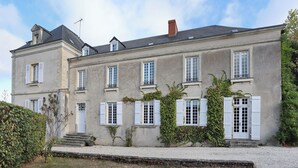 Um edifício de dois andares com fachada simétrica, várias janelas com persianas e um caminho de acesso de brita.