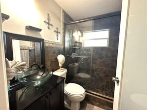 Et badeværelse med et glasafskærmet brusebad, en sort vask og et hvidt toilet.