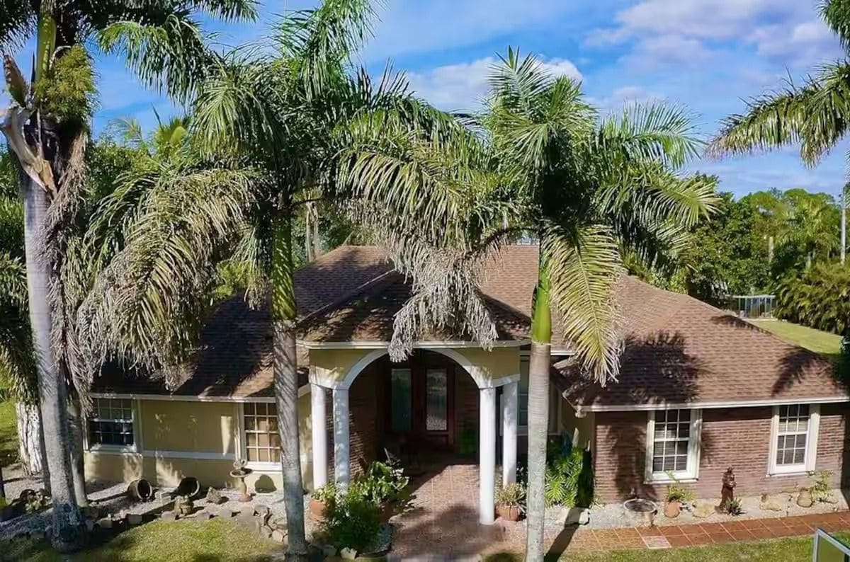 A single-story house with a brick exterior, a covered porch, and a well-maintained garden with palm trees.