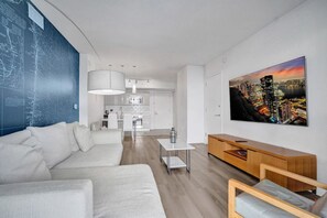 A modern living room with a sofa, a coffee table, and a TV on the wall. - Modern Spacious 1-BR APT / Beachwalk Resort (Hallandale Beach)