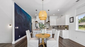 A modern kitchen with white cabinetry, a large blue abstract painting on the wall, and a round wooden table with white upholstered chairs. - Furnished Monthly- 3BR Rooftop- East Nashville (Nashville)