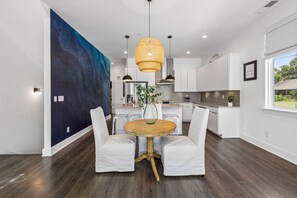 A modern kitchen with white cabinetry, a large blue abstract painting on the wall, and a round wooden table with white upholstered chairs. - Furnished Monthly- 3BR Rooftop- East Nashville (Nashville)