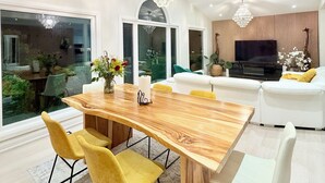 Uma sala de estar moderna com uma mesa de jantar de madeira, cadeiras amarelas, um sofá branco e uma grande TV de tela plana.