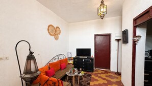 Een woonkamer met een bank, een televisie, een decoratief wandobject, een deur en een vloer met patroon.