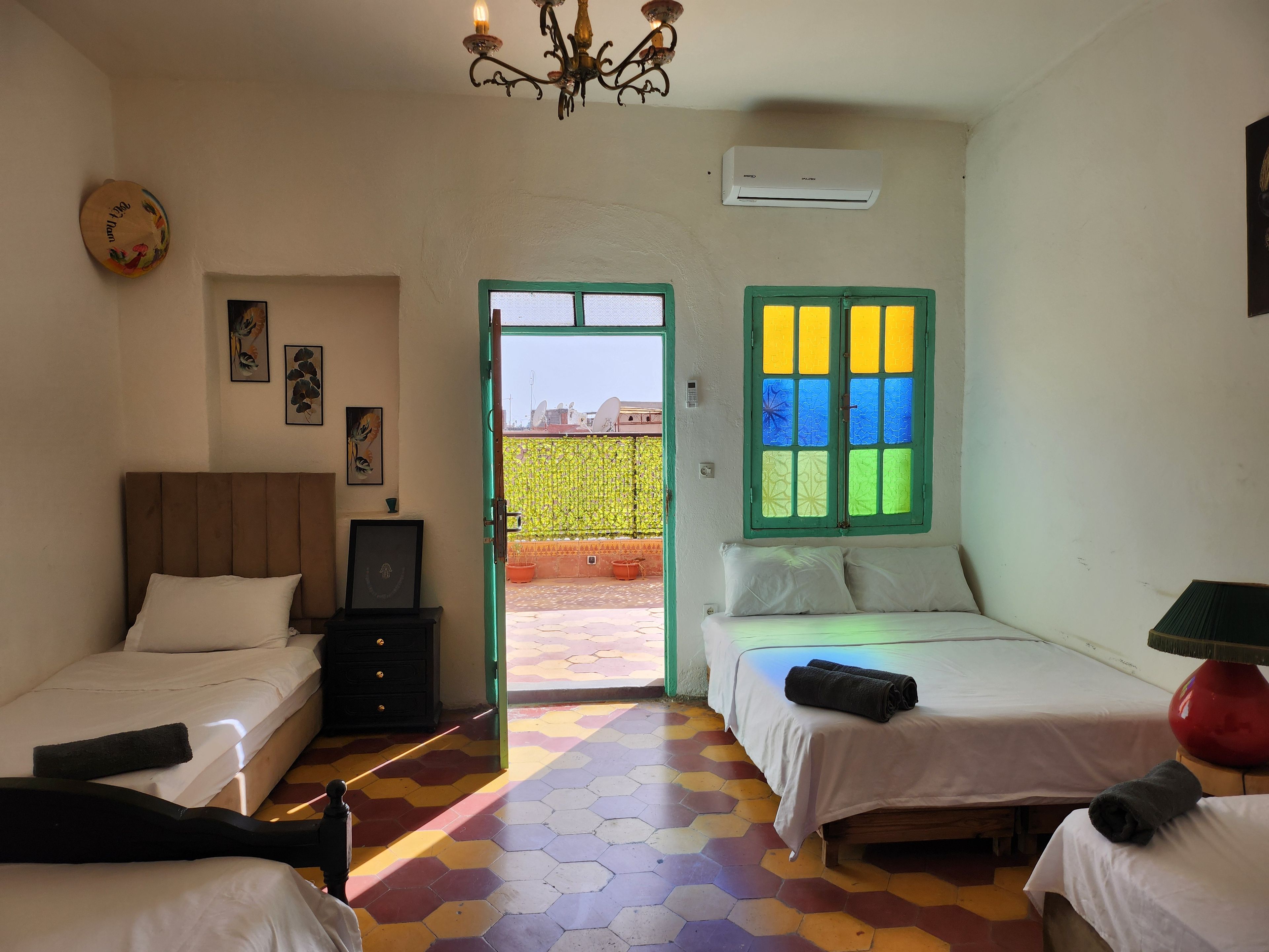 Une chambre d’hôtel avec deux lits, un lustre, un appareil de climatisation et une vue sur l’extérieur, visible à travers une porte.