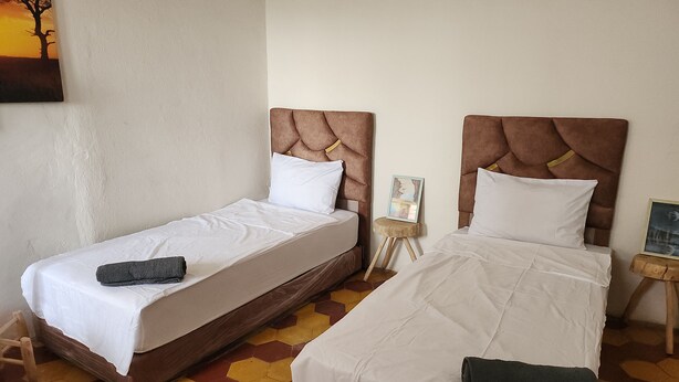 Een kamer met twee eenpersoonsbedden, elk met hoofdbord, witte beddengoed en een klein nachtkastje met een fotolijstje.