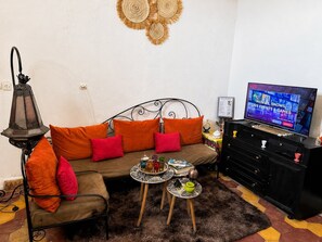 A cozy living room with a sofa, a television, a decorative wall hanging, and a small table with drinks. - 3-bedroom apartment with a private terrace, 5 minutes from Jemaa el-Fna (Marrakech)