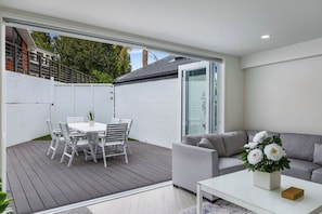 A modern patio with a dining table and chairs, a grey sofa, and a white coffee table. - Brand New 3BR in Remuera by Zodiak (Auckland)