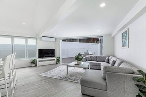 Ein modernes Wohnzimmer mit einem grauen Sofa, einem Flachbildfernseher und einem Essbereich mit Tisch und Stühlen.