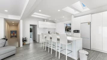 A modern kitchen with white cabinetry, a dining area with white chairs, and a grey sofa in a living room.