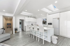 Een moderne keuken met witte kasten, een eethoek met witte stoelen en een grijze bank in een woonkamer.