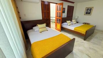Quarto de hotel com duas camas, cabeceira de madeira, colcha amarela e janela com cortinas.