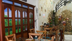 Ein Essbereich mit Holztischen und -stühlen, eine dekorative Wand mit einem Buddha-Bild und eine Steinwand mit Blumentöpfen.
