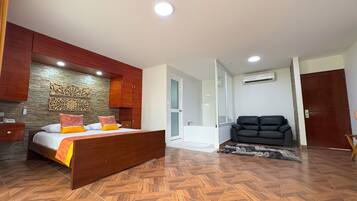Quarto com cama de madeira, sofá e banheiro com porta de vidro.