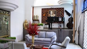 Ein Wohnzimmer mit einem grauen Sofa, einem roten Teppich und einem Klavier im Hintergrund.