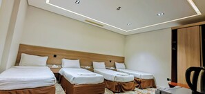 A hotel room with three single beds, a wooden headboard, a desk with a chair, and a ceiling with recessed lighting.