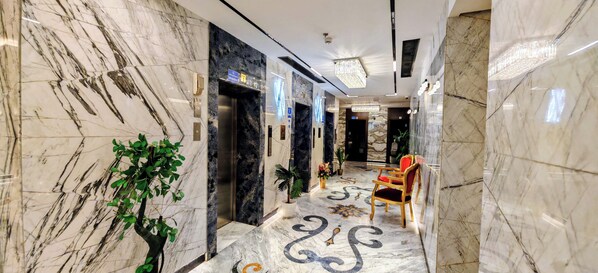 A marble-floored corridor with an elevator, a reception area with a red chair, and potted plants.