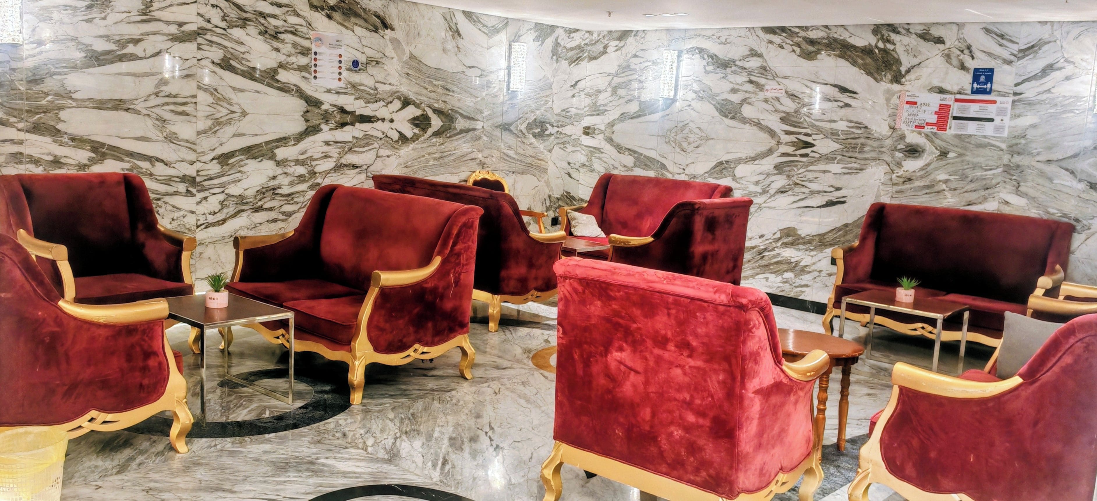 A seating area with red velvet chairs and gold accents, marble walls, and a clean, modern design.