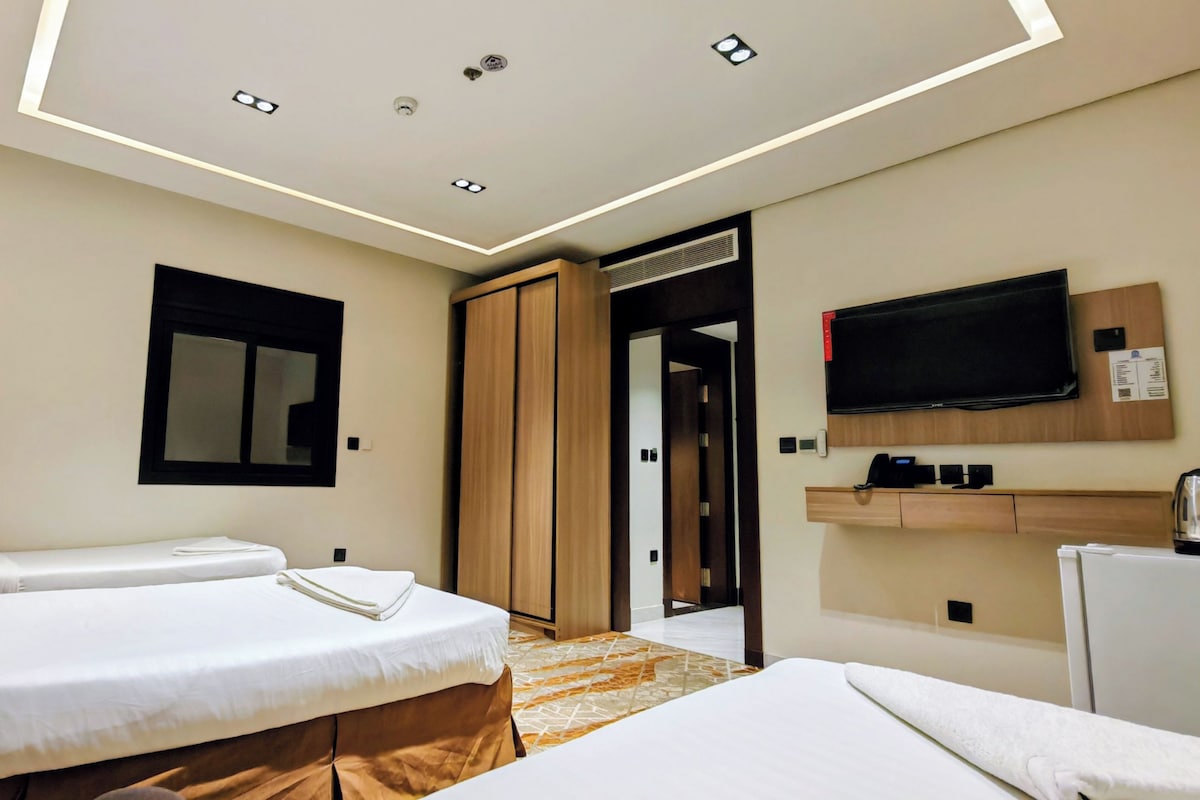 Ein Hotelzimmer mit zwei Betten, einem Fernseher, einer Minibar und einer Tür zu einem Badezimmer.