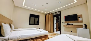 Ein Hotelzimmer mit zwei Betten, einem Fernseher, einer Minibar und einer Tür zu einem Badezimmer.