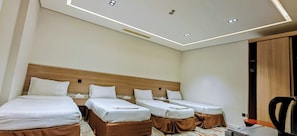 Ein Hotelzimmer mit drei Einzelbetten, einem Holz-Kopfteil, einem Schreibtisch mit Stuhl und einer Decke mit Einbaustrahlern.
