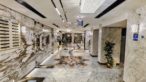 Corredor de hotel com paredes de mármore, piso estampado e balcão de recepção.