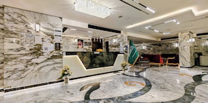 A hotel reception area with marble walls, a reception desk, a flag, and seating.