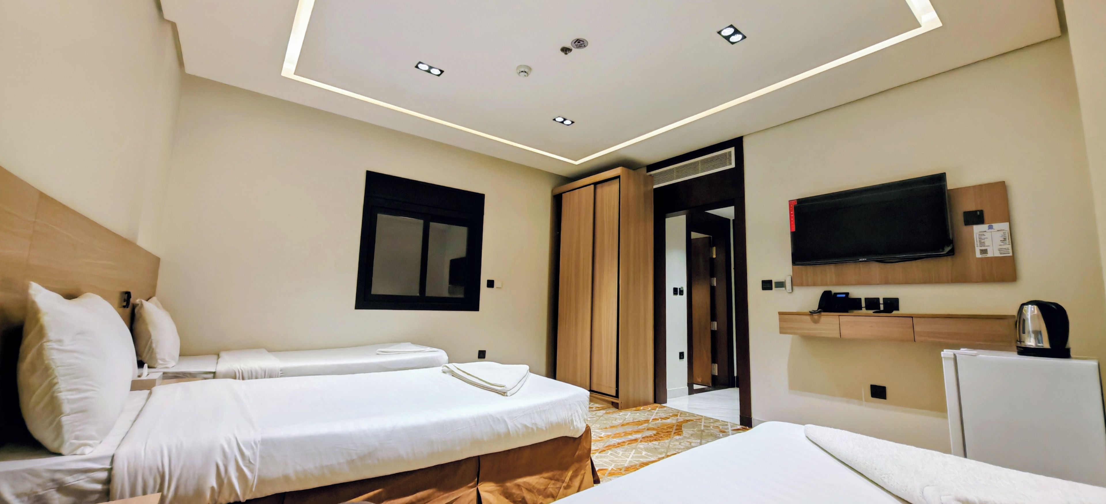 A hotel room with two beds, a television, a minibar, and a bathroom door.
