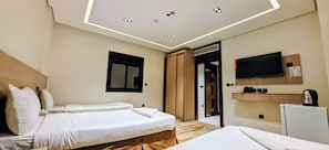 Ein Hotelzimmer mit zwei Betten, einem Fernseher, einer Minibar und einer Badezimmertür.