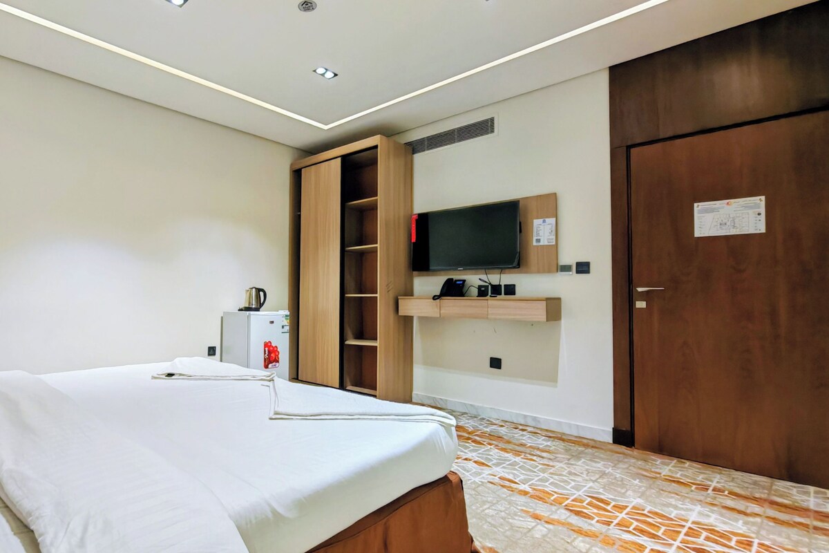 Ein Hotelzimmer mit Bett, Wandfernseher, Kleiderschrank und einer kleinen Küchenzeile.