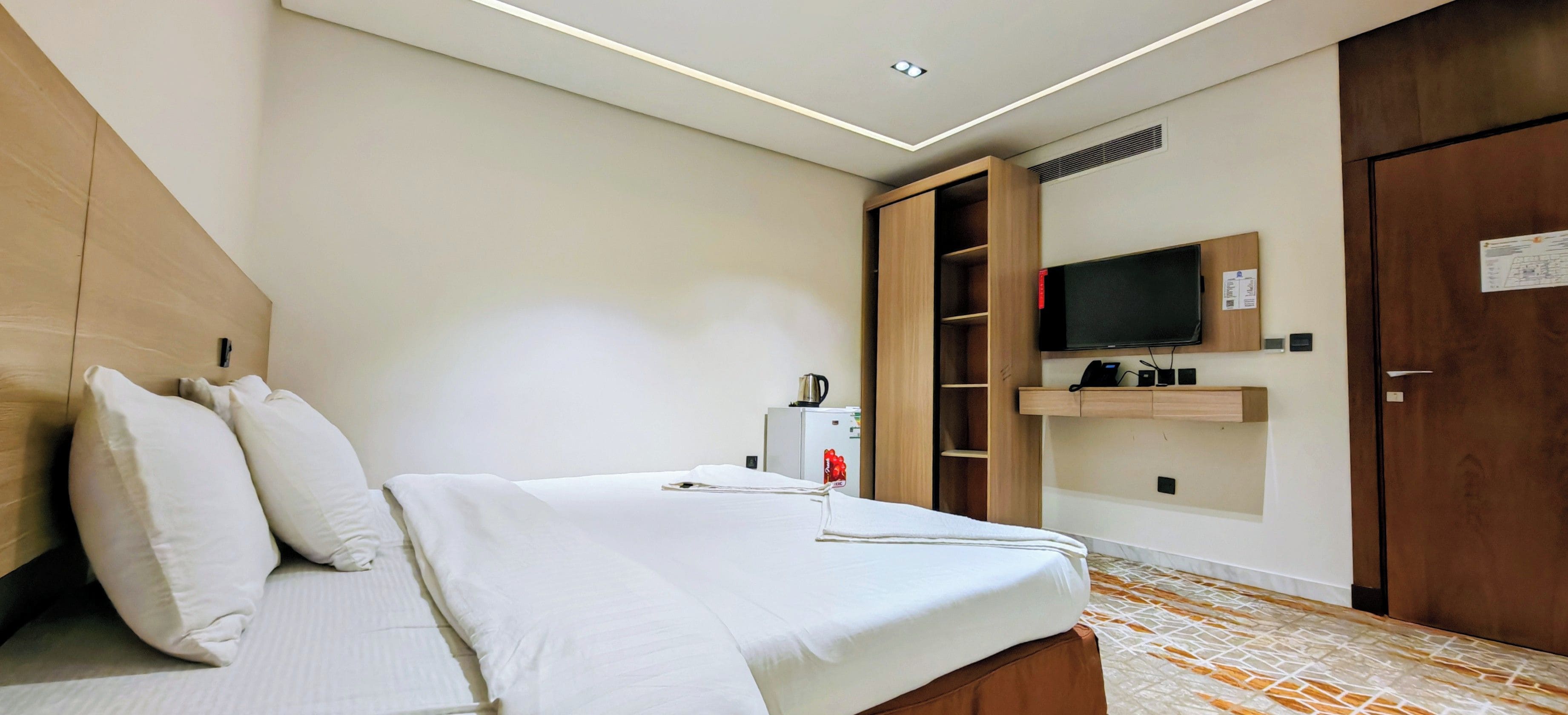 Une chambre d’hôtel équipée d’un lit, d’un téléviseur fixé au mur, d’un mini-bar et d’une armoire en bois.