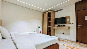 Une chambre d’hôtel équipée d’un lit, d’un téléviseur fixé au mur, d’un mini-bar et d’une armoire en bois.