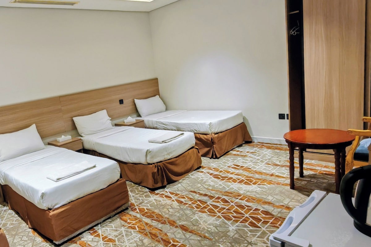 Ein Hotelzimmer mit drei Einzelbetten, einem kleinen Tisch und einem Stuhl.