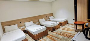 A hotel room with three single beds, a small table, and a chair.