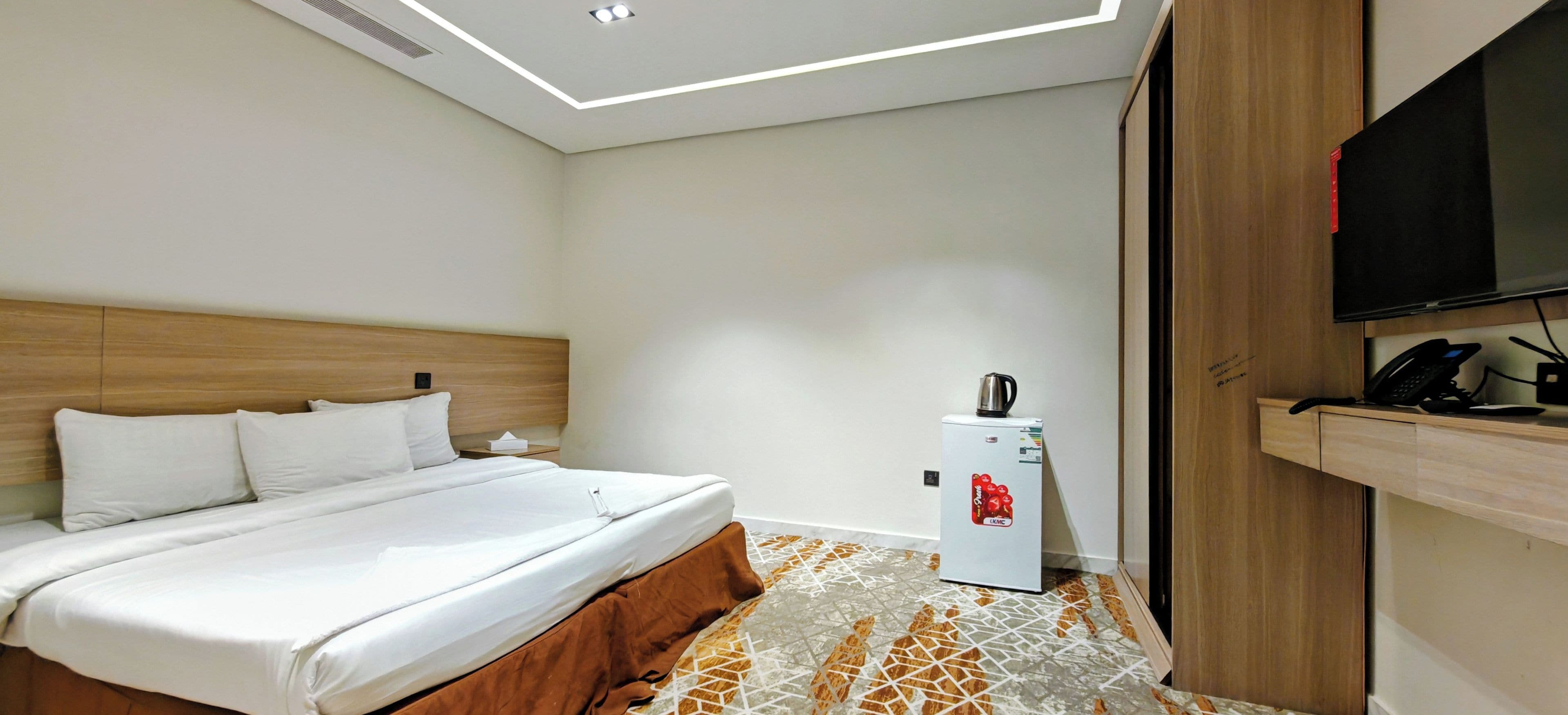 Une chambre d’hôtel équipée d’un lit, d’un petit réfrigérateur, d’une télévision et d’une armoire en bois.