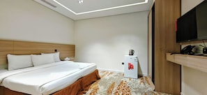 A hotel room with a bed, a small refrigerator, a television, and a wooden wardrobe.