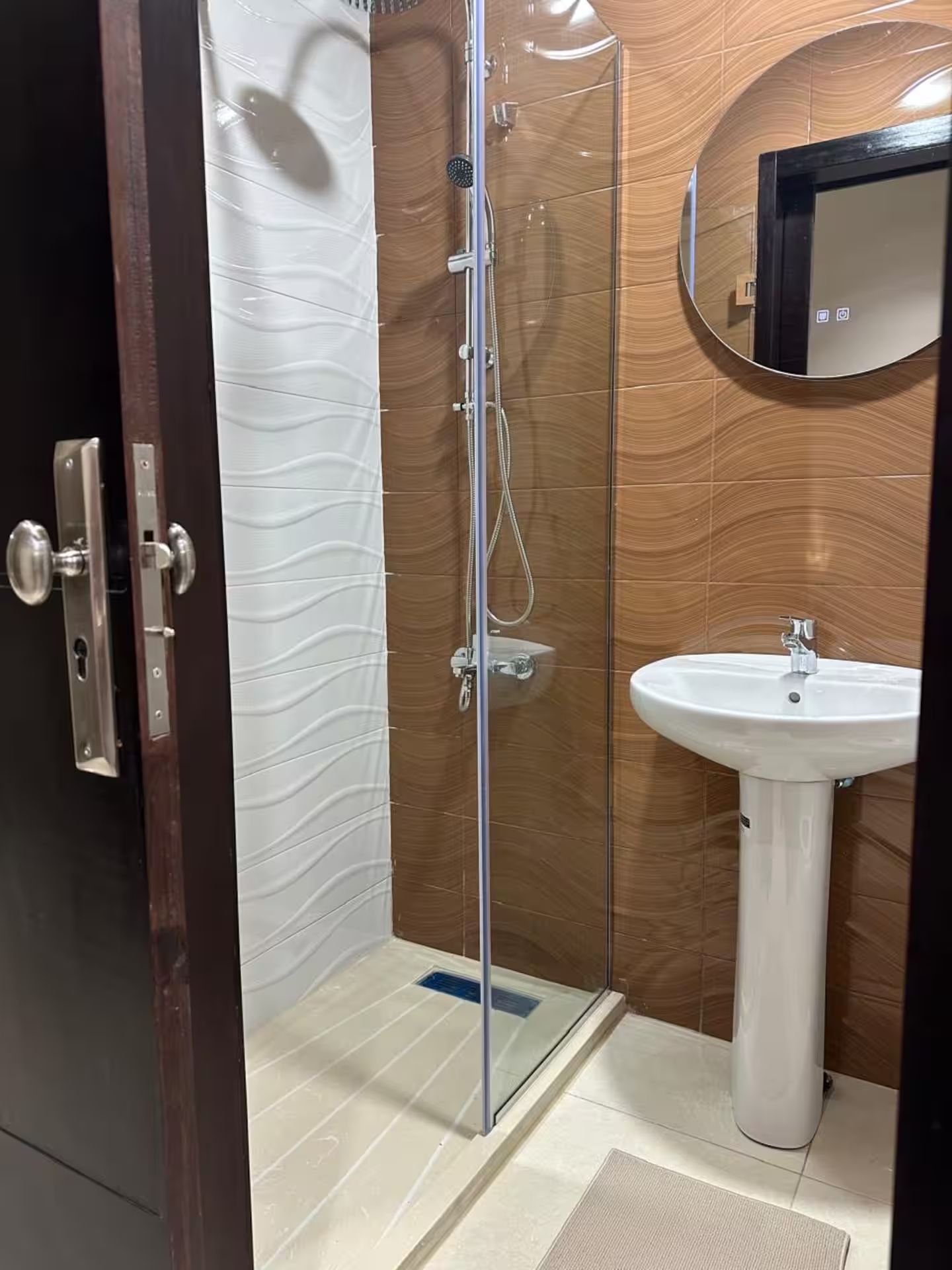 Une salle de bain avec une douche à parois de verre, un lavabo blanc et un mur en bois.