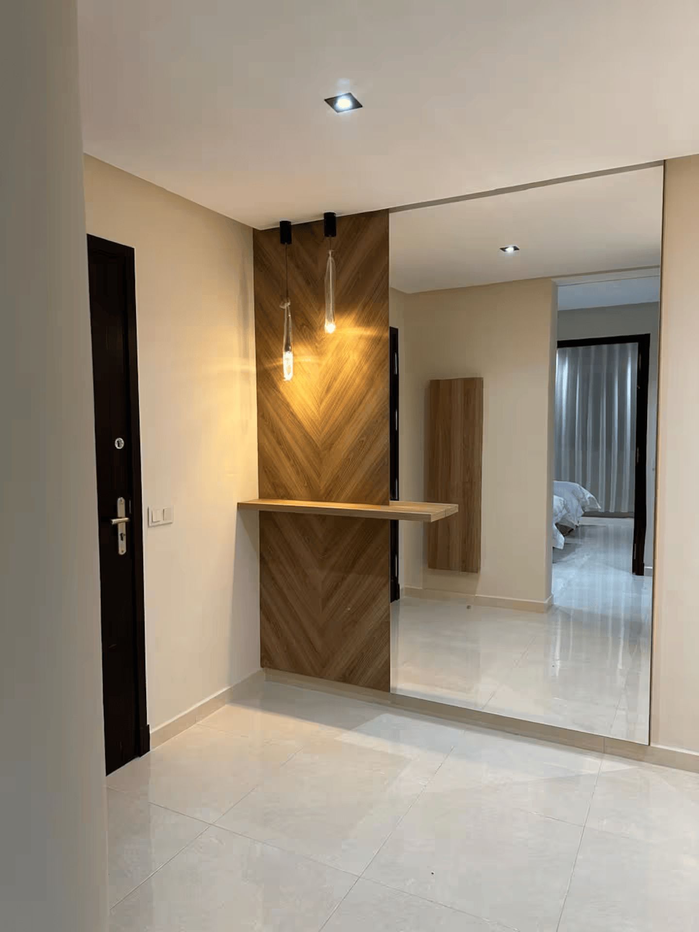 Un intérieur moderne avec un mur d’accent en bois, des spots encastrés au plafond et un grand miroir qui reflète une chambre à coucher.