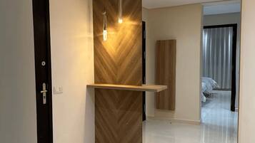 Un intérieur moderne avec un mur d’accent en bois, des spots encastrés au plafond et un grand miroir qui reflète une chambre à coucher.