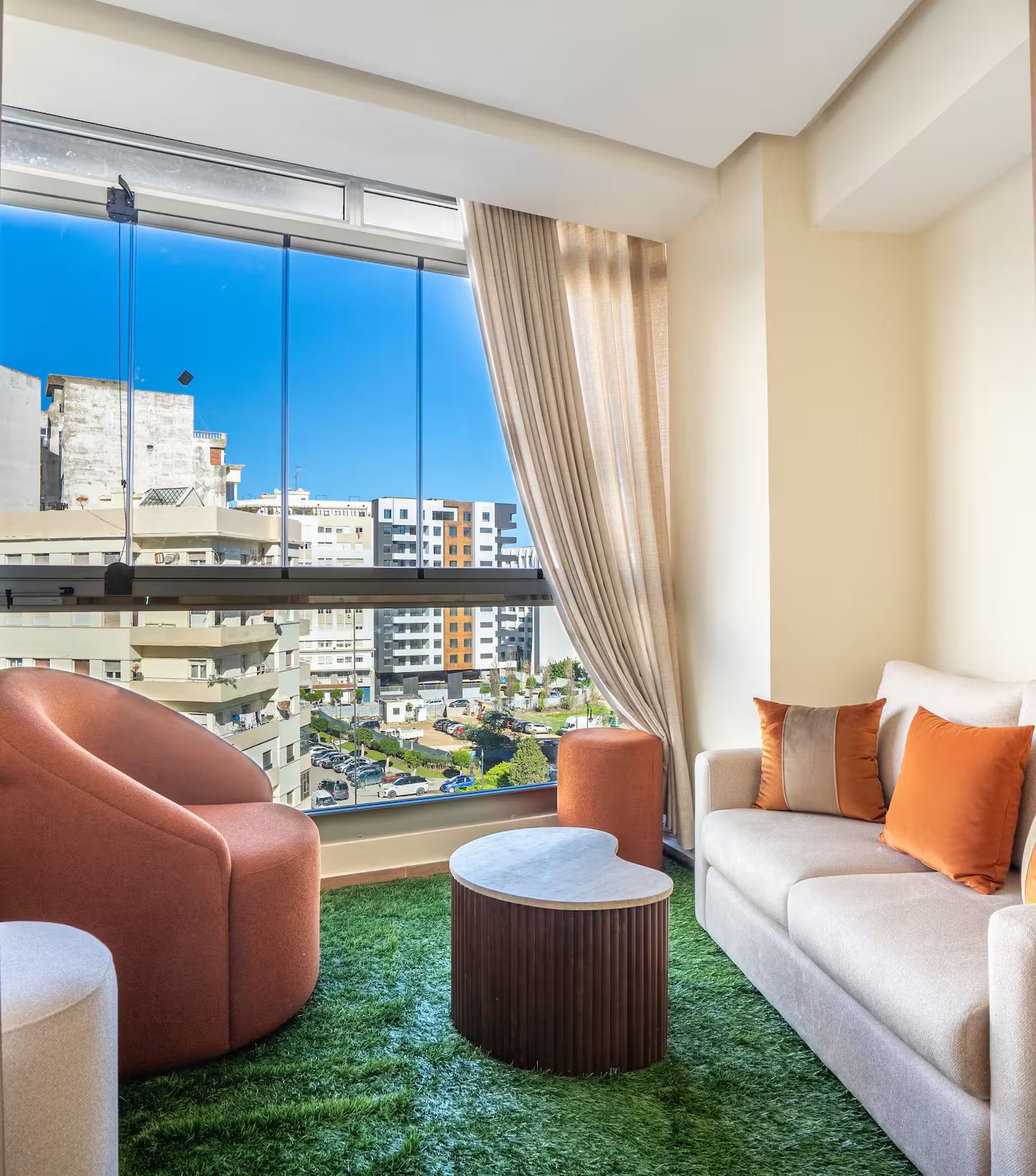 Un salon moderne avec vue sur le paysage urbain, grâce à de grandes fenêtres, une table basse ronde et deux canapés.