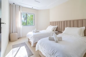 A hotel room with two beds, a window with curtains, a bedside table, and a small ottoman. - Experience Modernity Beachside & Parking in Pleasant 2-bedroom apartment with AC (Tangier)