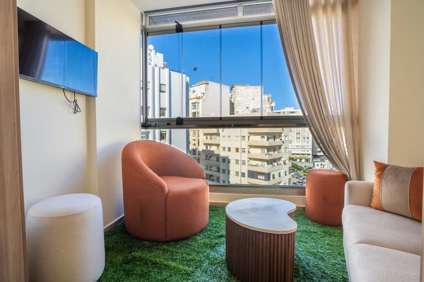 Ein modernes Wohnzimmer mit großem Fenster, einem Flachbildfernseher und Blick auf eine Stadtlandschaft.