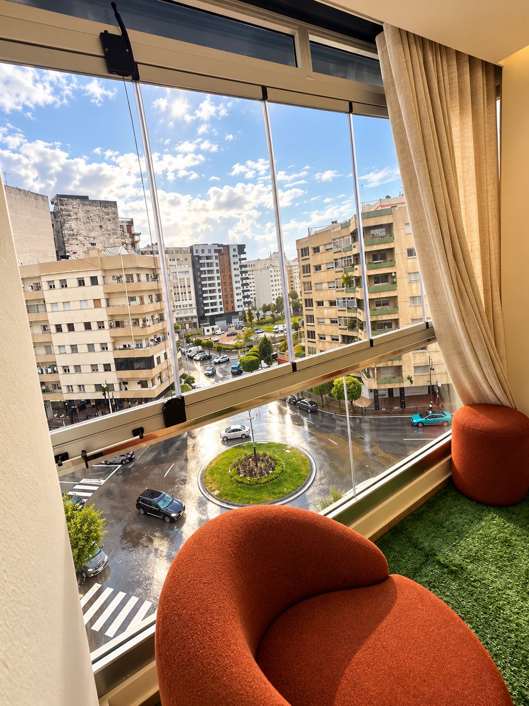Una stanza con un'ampia finestra che si affaccia su una vista urbana, una rotonda e una zona verde.