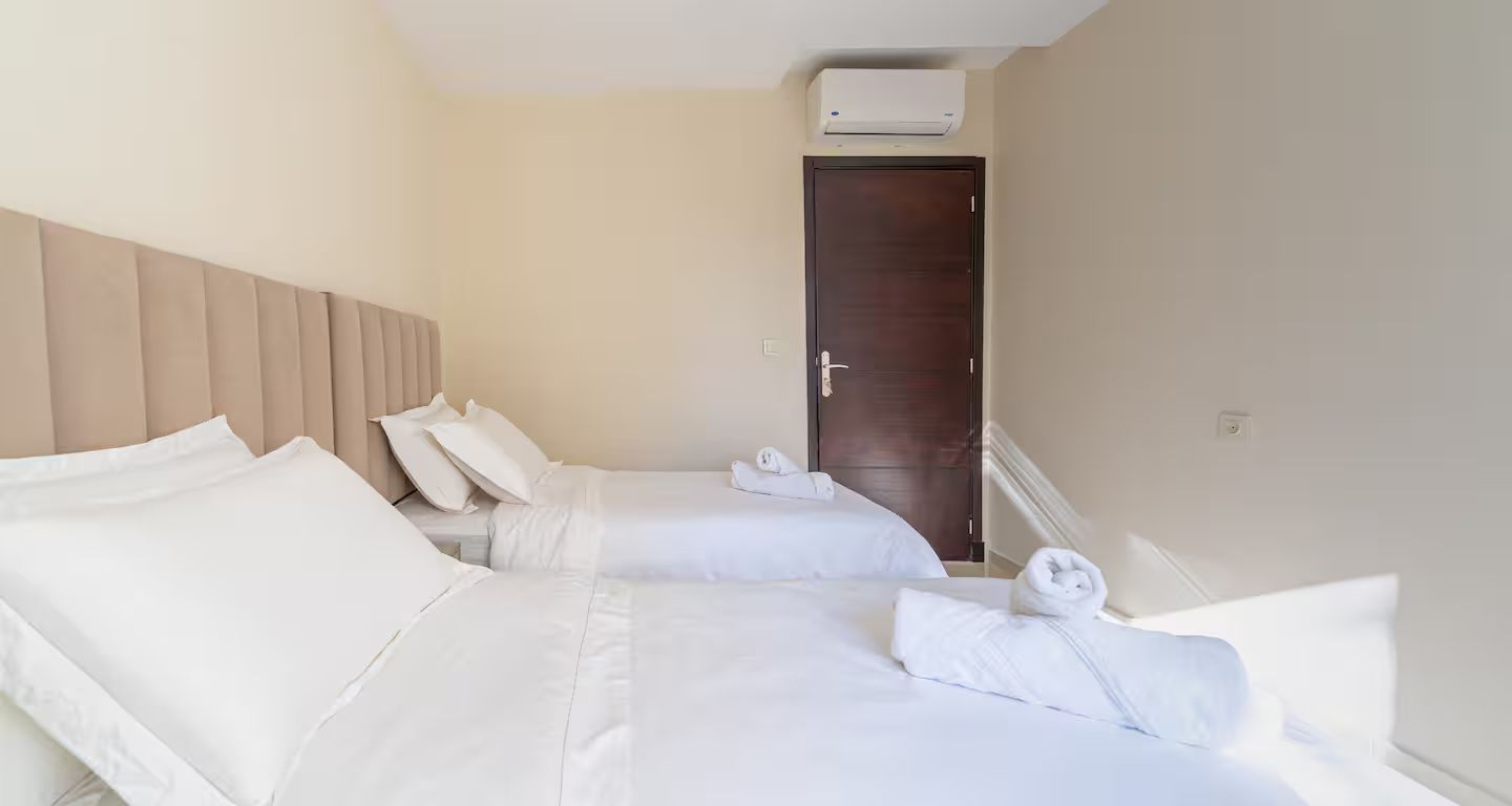 Habitació d'hotel amb dos llits, una porta de fusta i un aparell d'aire condicionat.
