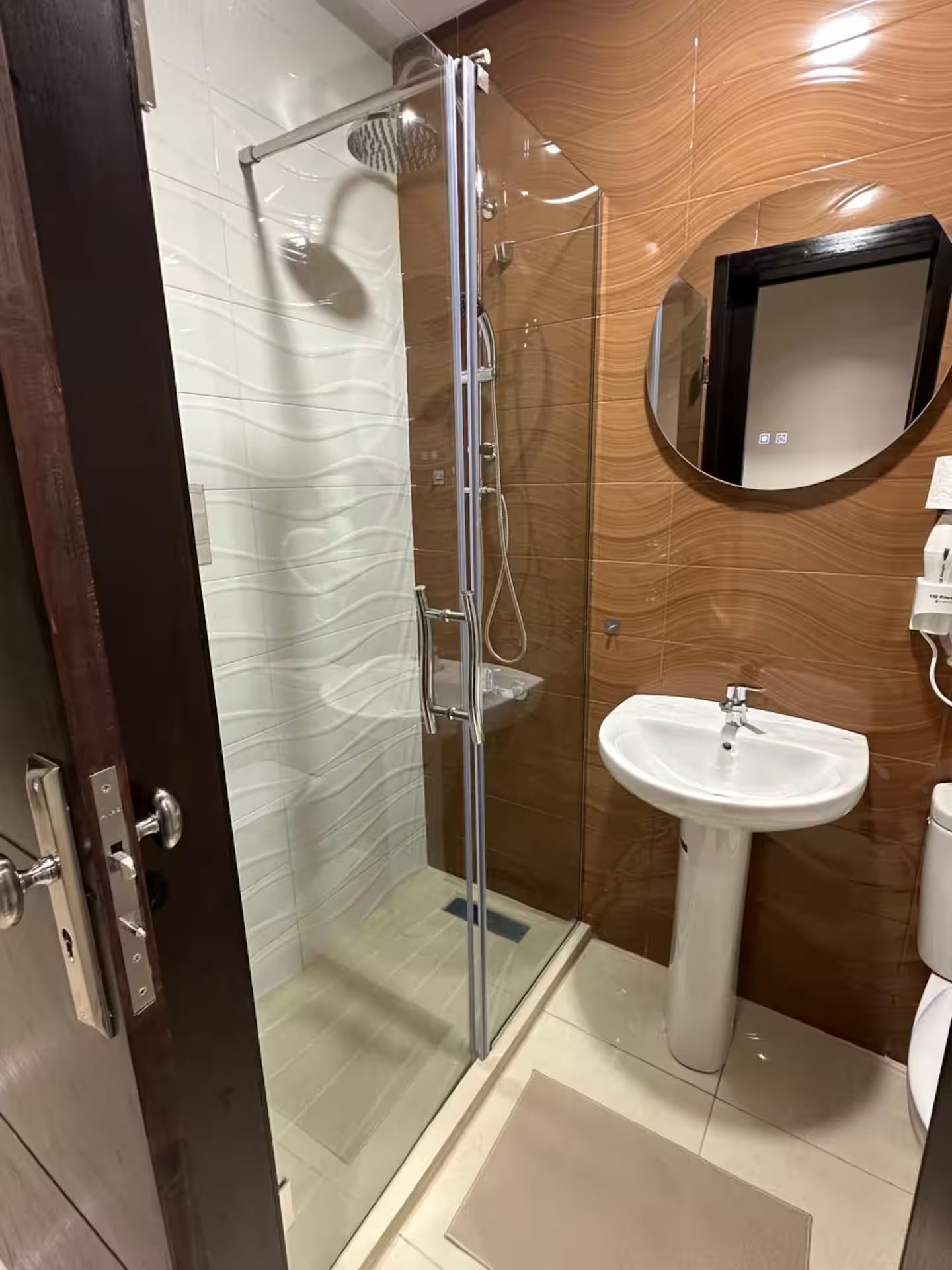 Une salle de bain moderne avec une douche à parois de verre, un lavabo sur colonne blanc et un panneau mural en bois.