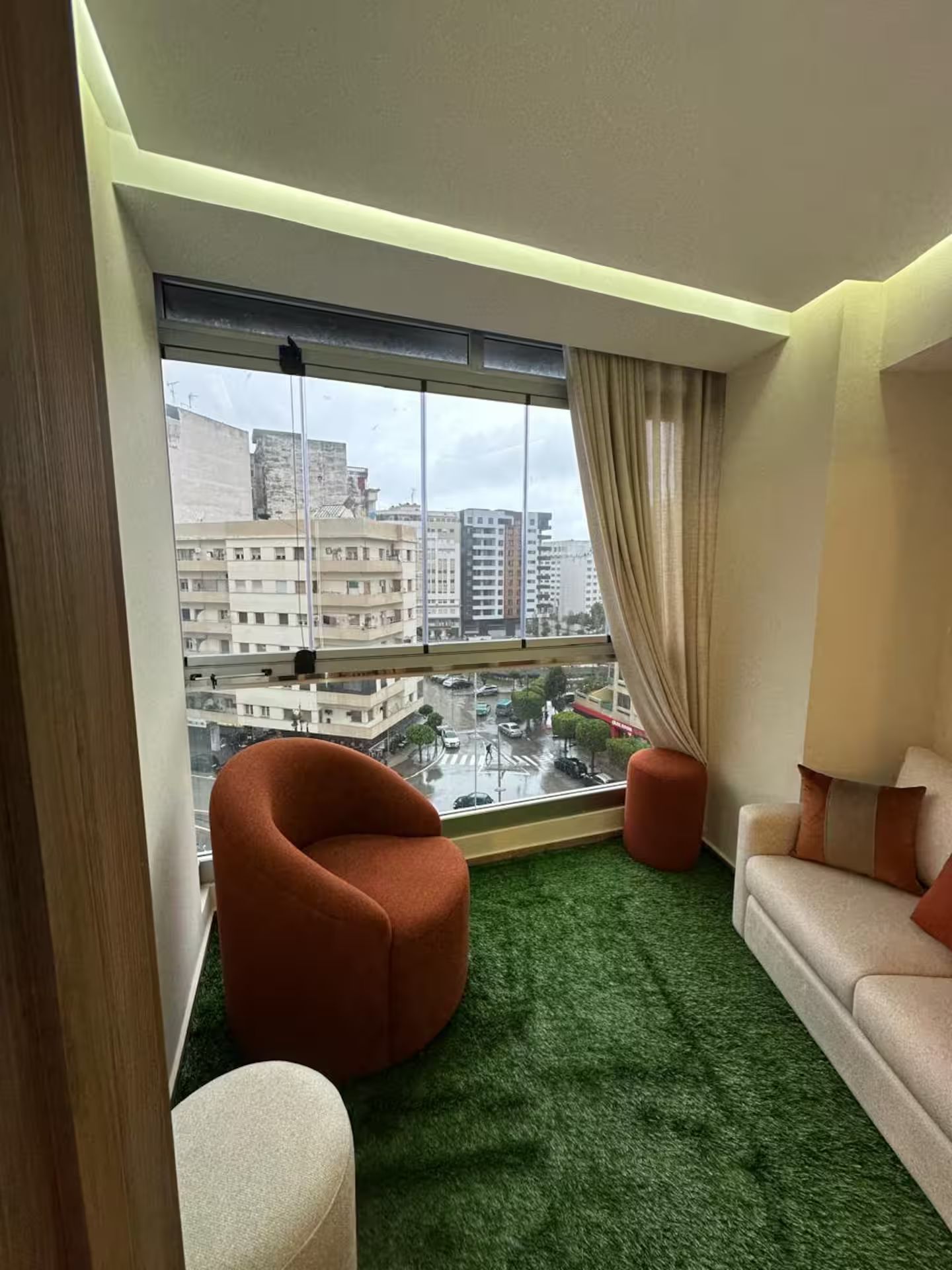 Un saló modern amb una finestra gran, una catifa verda i una vista a la ciutat.