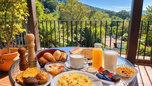 A breakfast table with various foods and drinks on a balcony with a scenic view.
