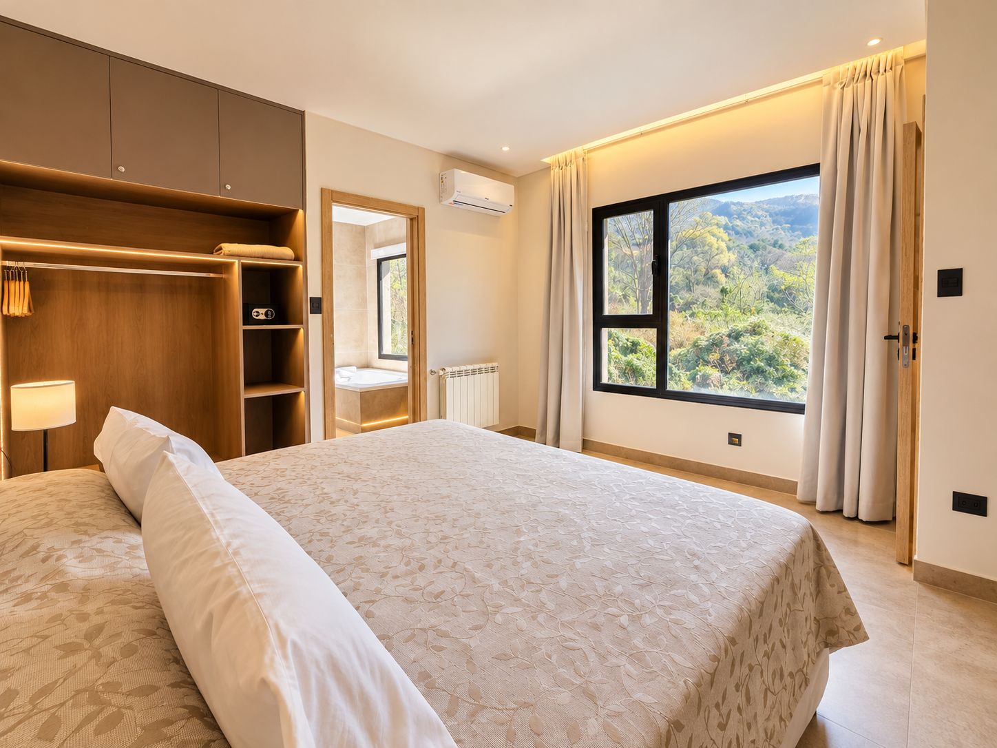 A hotel room with a large bed, a walk-in closet, a window with a view of greenery, and an air conditioning unit.