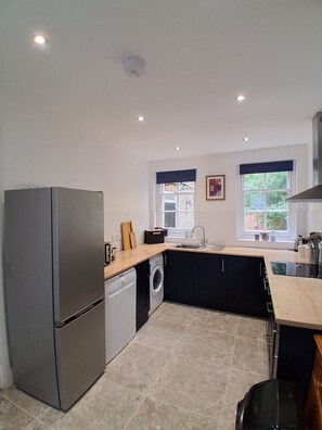 A compact kitchen with a refrigerator, washing machine, and a sink. - Cottage Two (Dover)